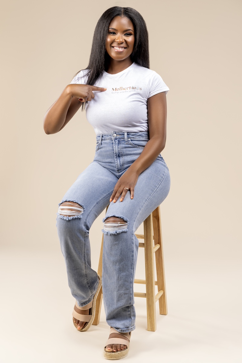 Kirsten_Smith | Motherhues Kirsten smith sitting on stool wearing MotherHues tshirt and pointing at logo