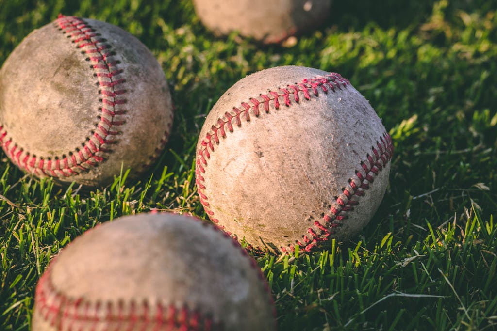 Photo by Steshka Willems | Motherhues Close Up Photography of Four Baseballs on Green Lawn Grasses