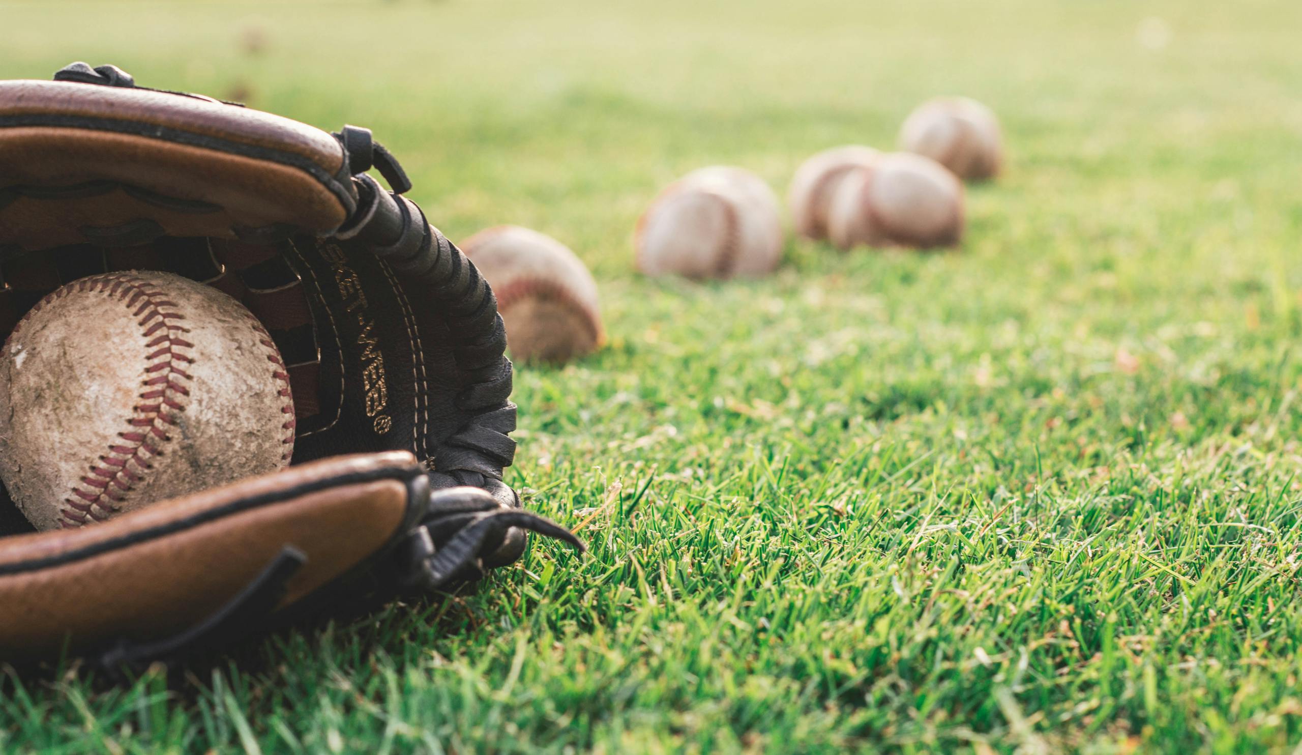 Photo by Steshka Willems | Motherhues A close-up of a baseball glove with balls on a green field, symbolizing outdoor sports.