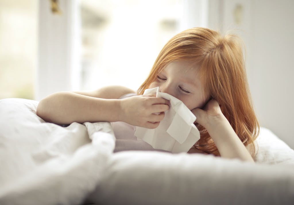 Photo by Andrea Piacquadio | Motherhues Redheaded child resting in bed, wiping nose with tissue, unwell with flu-like symptoms.