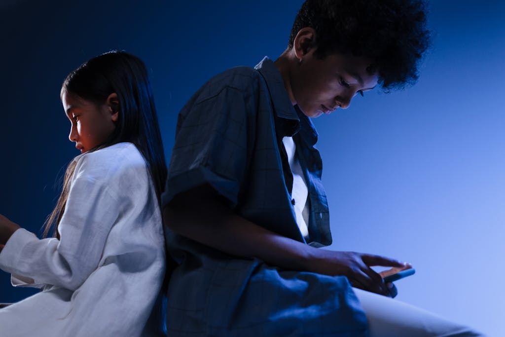 Photo by Ron Lach | Motherhues Young boy and girl using mobile devices in a conceptual studio setting with blue lighting.