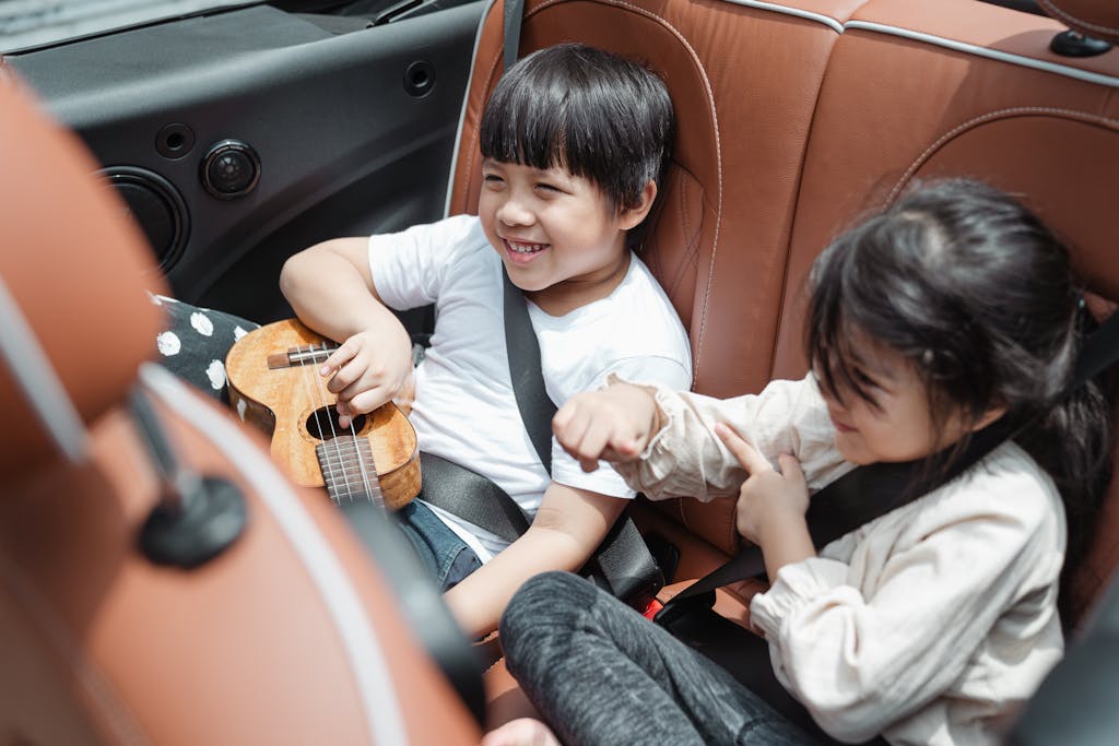 Photo by Ketut Subiyanto | Motherhues From above smiling ethnic boy and girl in casual outfits sitting fastened in passenger seats with ukulele during road trip together