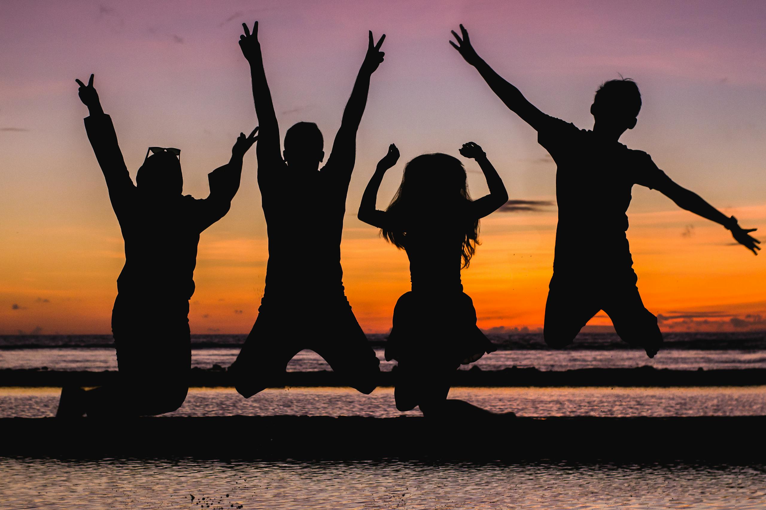Photo by Vija Rindo Pratama | Motherhues Silhouette of friends jumping on the beach at sunset, celebrating summer fun.