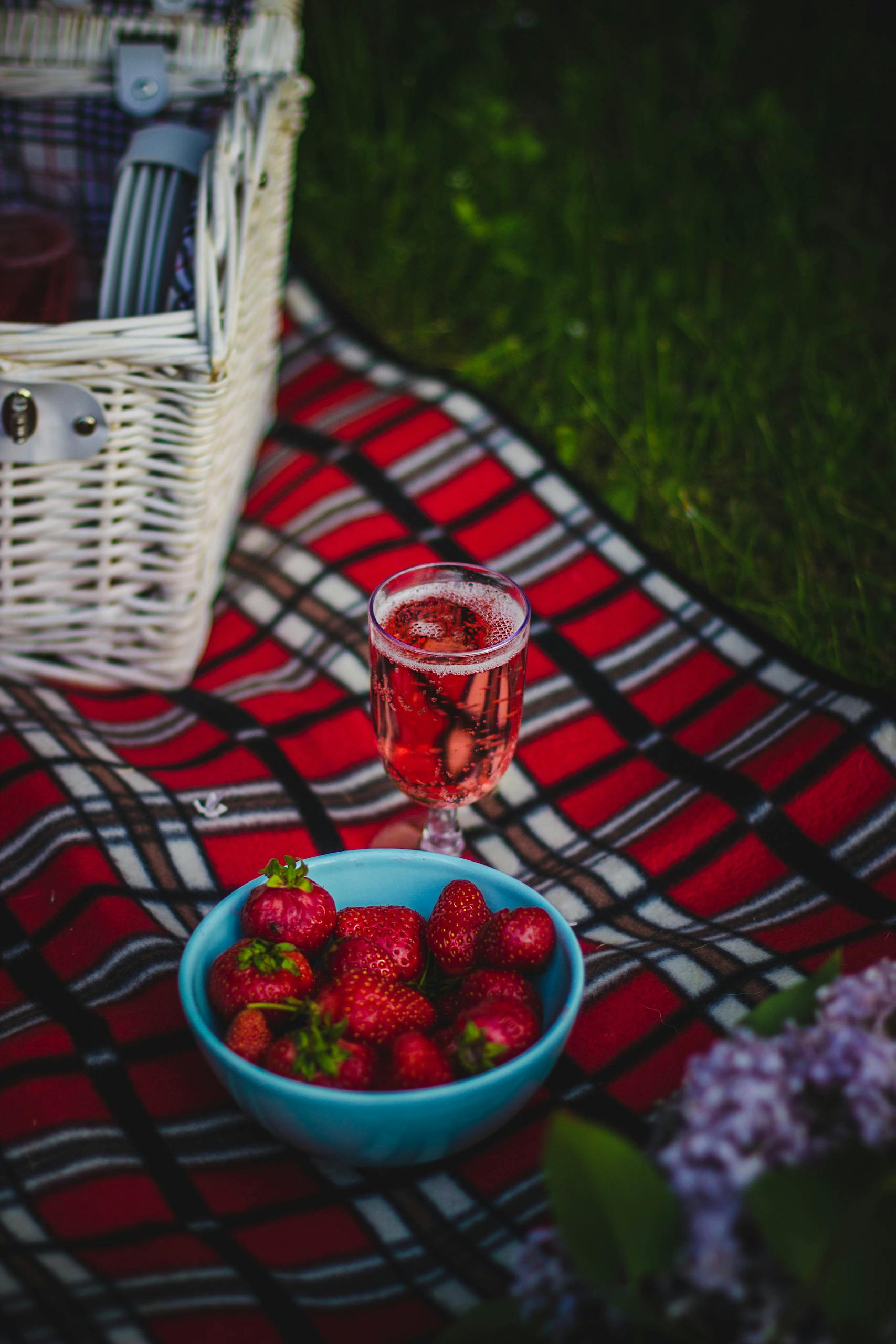 Photo by Valeria Boltneva | Motherhues A picnic scene with strawberries in a bowl and a sparkling drink on a plaid blanket outdoors.