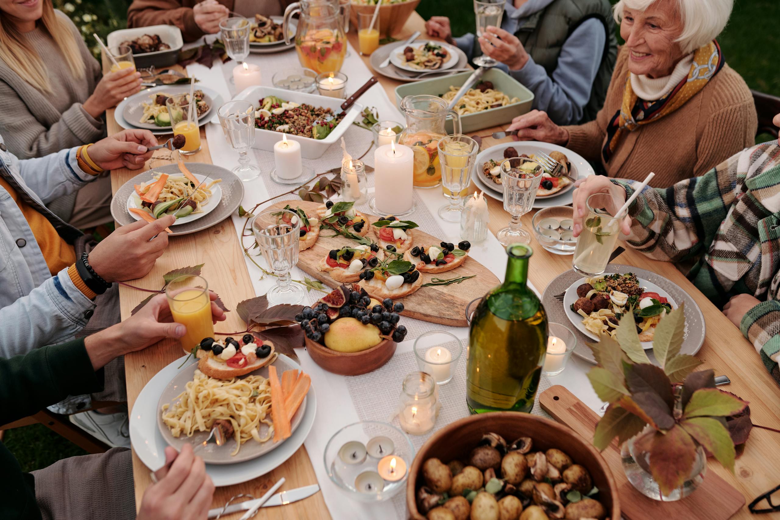 Photo by Askar Abayev | Motherhues From above crop people enjoying festive dinner with snacks at garden table with candles burning
