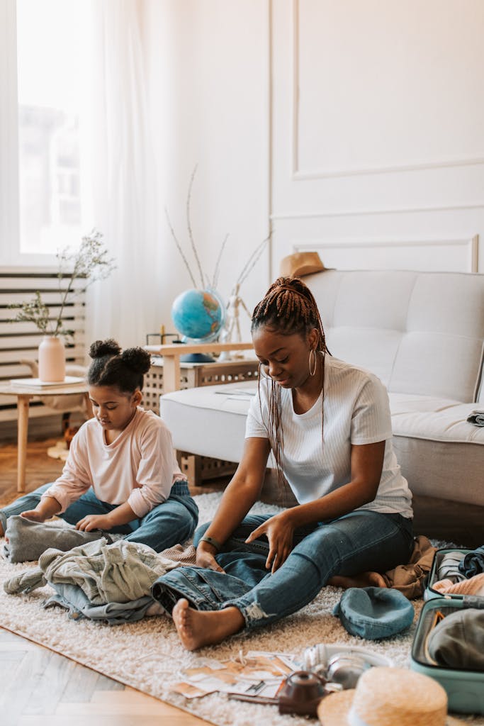 Photo by Vlada Karpovich | Motherhues A mother and daughter sit on the floor, packing clothes in a living room.