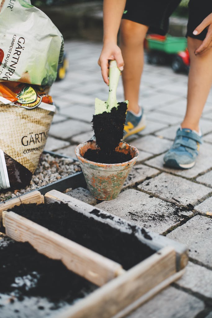 Photo by Markus Spiske | Motherhues A child actively participates in gardening by shoveling soil into a pot on a patio in the spring.