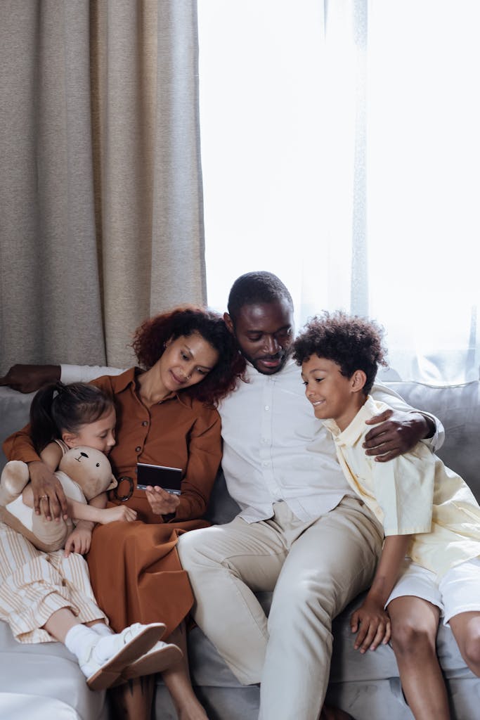 Photo by Ron Lach | Motherhues A loving family of four sitting on a couch indoors sharing a joyful moment.