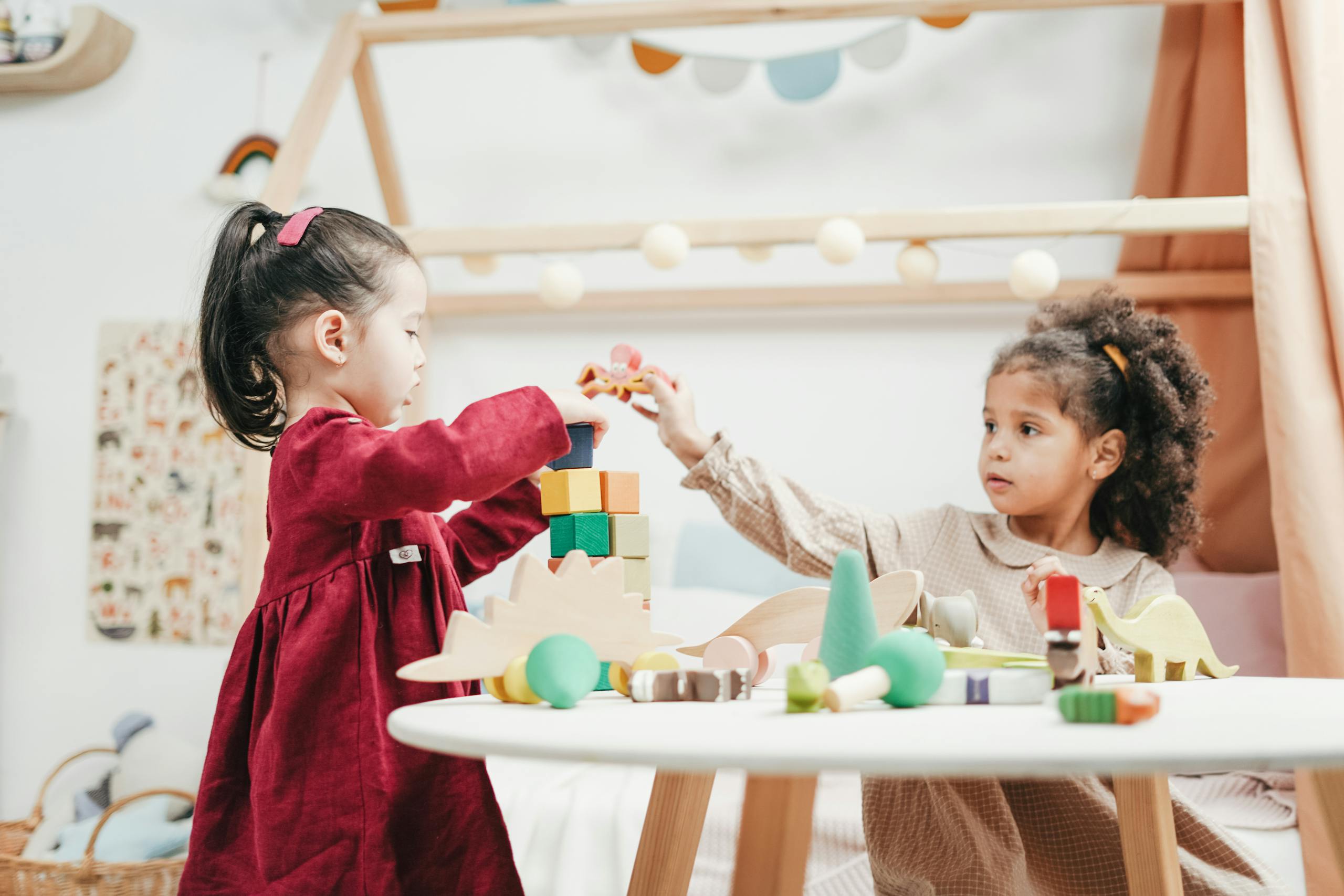 Photo by cottonbro studio | Motherhues Two young girls enjoying playtime with wooden toys indoors in a warm, colorful playroom.