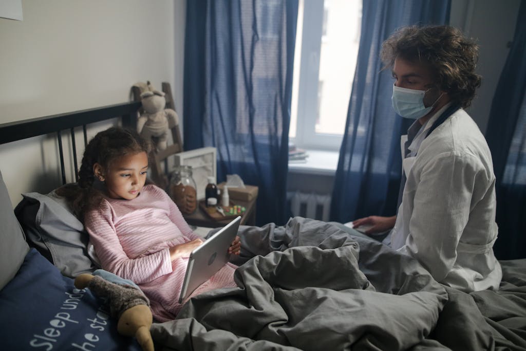Photo by cottonbro studio | Motherhues Young girl with a tablet in bed as a doctor attends in a cozy bedroom setting.