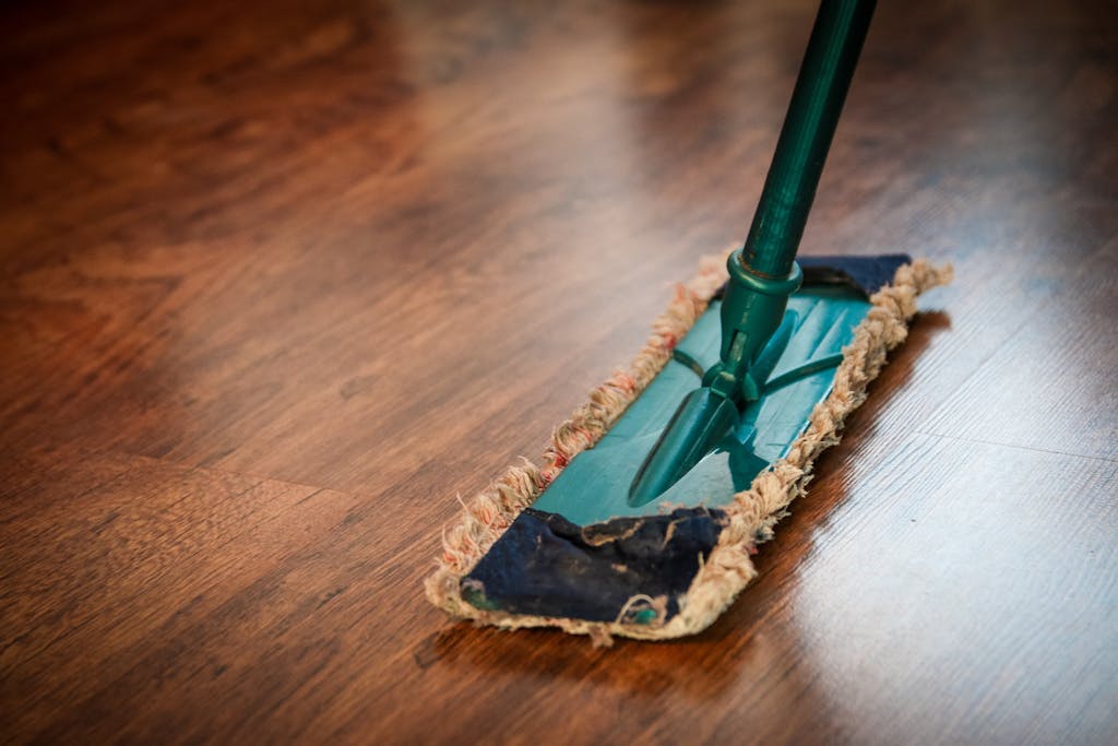 Photo by Pixabay | Motherhues A detailed view of a mop cleaning a wooden floor, showing texture and pattern.