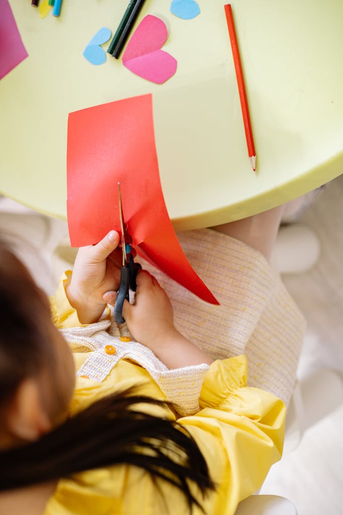 Photo by Yan Krukau | Motherhues Top view of a girl cutting colored paper during a creative arts and crafts session indoors.