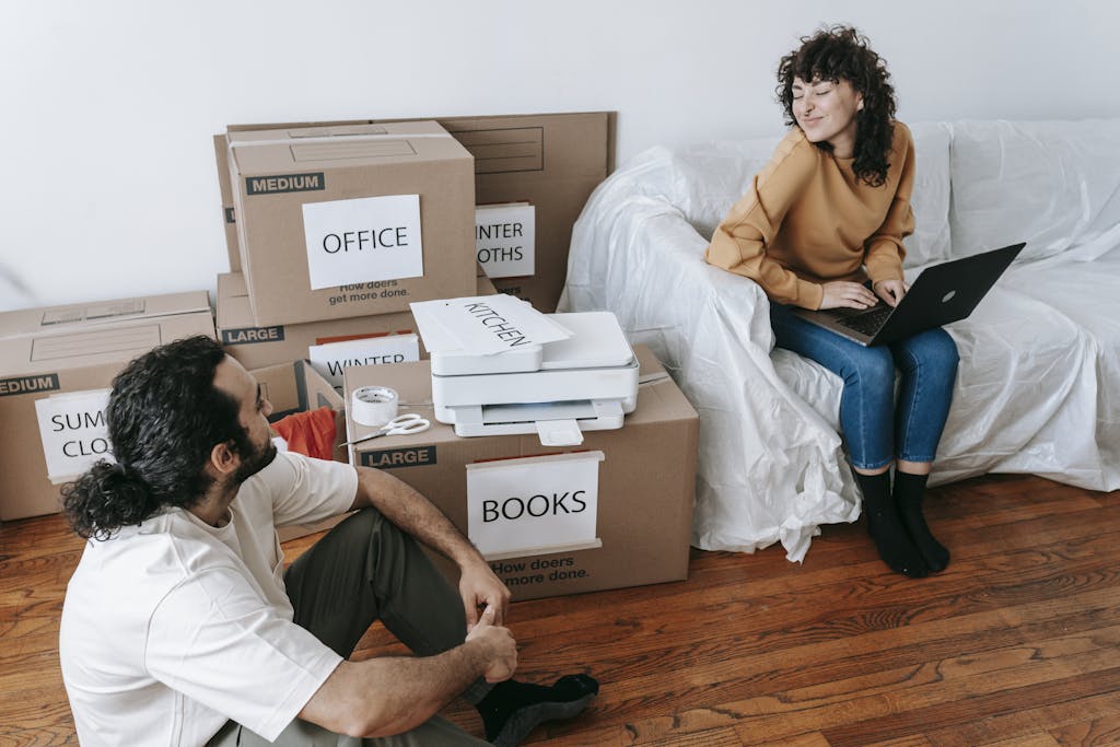 Photo by Blue Bird | Motherhues Young couple organizing boxes and relaxing with laptop during moving day indoors.