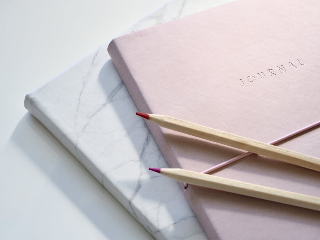 Photo by Jess Bailey Designs | Motherhues Close-up of a pink journal with pencils on a marble top. Perfect for note-taking or planning.