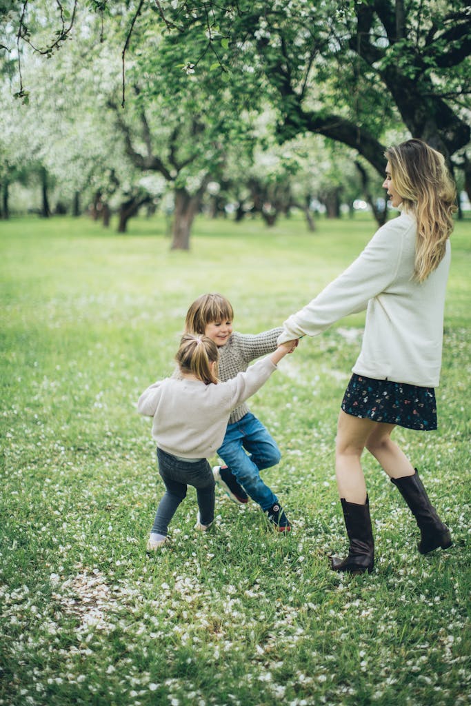 Photo by Elina Fairytale | Motherhues Joyful mother with two kids playing in a blossoming park, capturing a moment of springtime fun and togetherness.